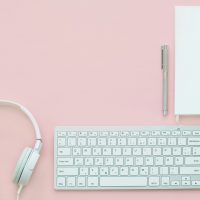 Plain Language. A white keyboard and white headphones on a pastel pink background.