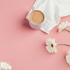Copy Editing. Copy Editor. A small cup of coffee on a pastel pink background surrounded by white flowers.